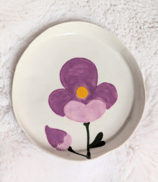 Round ceramic plate with a purple flower design on a white background